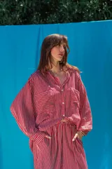 Camisa de fibrana con diseño de rayas verticales rojas y blancas, corte oversize, mangas largas abullonadas, cuello camisero y bolsillos frontales con solapa.