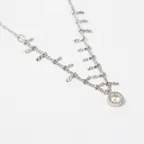 Colgante de cadena fina de acero con múltiples dijes pequeños en forma de barra y un dije central circular con cristal engastado.