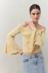 Top tejido color crema con escote off-shoulder y mangas largas acampanadas con terminación trabajada.