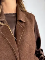 Chaleco largo color beige, con cuello solapa, un botón frontal y dos bolsillos de parche. Presenta costuras decorativas en contraste.