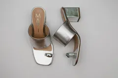 Sandalias de cuero color bronce con taco cuadrado y tira ancha sobre el empeine. Presentan un aro metálico plateado que separa el dedo gordo del resto.