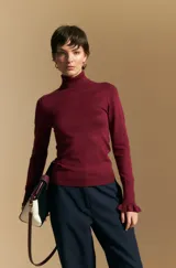 Polera de tejido fino color negro, con cuello alto y mangas largas con terminación sutilmente fruncida. Diseño ajustado al cuerpo.