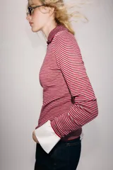 Jersey de punto confeccionado en hilatura con lana, con diseño de rayas horizontales en tonos rojo y gris. Presenta cuello solapa, escote en V y detalle de botones decorativos en el cuello y la solapa.