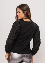 Blusa negra de tejido de punto acanalado, con cuello redondo y mangas largas abullonadas de tela semitransparente. Presenta una hilera vertical de pequeñas cuentas plateadas en el frente.