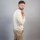 Buzo de punto color beige con cuello alto y medio cierre frontal.