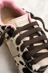 Zapatillas bajas de cuero con estampado de vaca en blanco y negro, cordones marrones y suela de goma color caramelo.