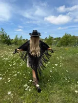 Ruana tejida a mano en lana merino, de color negro, con diseño calado y terminación de flecos largos en todo el contorno.