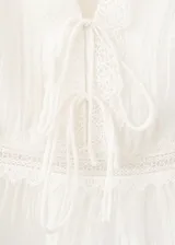 Top blanco sin mangas, con escote en V pronunciado, detalles de encaje y lazos ajustables en el frente. Presenta diseño corto y ligero con dobladillo con vuelo.
