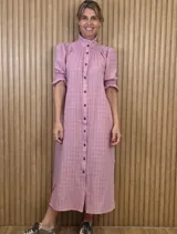 Vestido midi rosado con diseño a cuadros sutiles, cuello alto con volado, botonadura frontal completa, mangas cortas abullonadas con puños elásticos fruncidos y corte recto de largo midi.