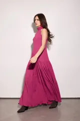 Vestido largo fucsia con escote halter y espalda baja. Tiene volado en el cuello y maxi volado en la cadera.