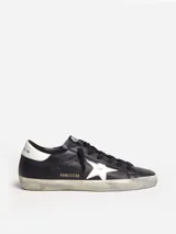 Zapatillas urbanas Golden Goose modelo Super-Star, color negro con estrella blanca en el lateral, detalle trasero en cuero blanco y suela con efecto desgastado.