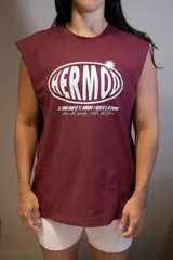 Musculosa sin mangas color bordó con cuello redondo. Estampado frontal en blanco con la palabra "HERMD" en un óvalo con efecto 3D y texto pequeño debajo que dice "el amor mueve el mundo y hasta el olimpo vibras del pasado. estilo del futuro".