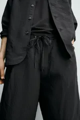 Bermuda relaxed fit de color negro, confeccionada en tejido fluido con viscosa y modal. Presenta cintura elástica ajustable con cordón, pliegues en el delantero, bolsillos frontales y bolsillos traseros de vivo.