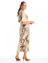 Vestido maxi de crepe color beige con estampado floral en tonos marrones y negros. Presenta cuello a la base, escote en V, abertura central con botones y cintura con lazo de ajuste y hebilla.