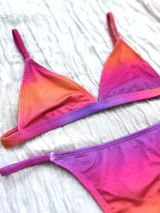 Conjunto de bikini con corpiño triangular fijo y bombacha colaless regulable, con estampado degradado en tonos naranja, rosado y violeta.
