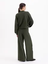 Pantalón de corte recto y silueta holgada, confeccionado en tejido rústico de algodón color verde militar. Presenta cintura con elástico interno y detalles de broches metálicos a presión en los laterales.