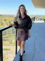 Camisa de color marrón oscuro con cuello clásico y mangas abullonadas con puños elásticos. Presenta un corte holgado y cierre frontal con botones.