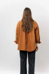 Sobrecamisa de gabardina liviana color crema, con corte oversize, cuello clásico, cierre frontal con botones a presión y dos bolsillos delanteros con solapa.