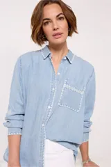 Camisa celeste de denim tencel, de corte holgado, con cuello clásico, cierre frontal con botones y bolsillo en el pecho con detalle bordado.