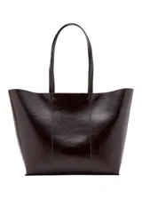 Bolso tipo shopper de gran tamaño en color marrón oscuro, con acabado brillante y textura lisa. Presenta un diseño minimalista con costuras visibles y estructura flexible.