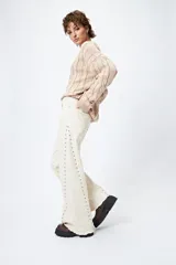 Pantalón de denim color crudo con corte wide leg, ruedo desflecado y detalle de tachas metálicas a lo largo de las costuras laterales.