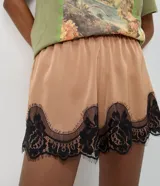 Short de satén color beige con acabado brillante, corte holgado, cintura elástica y detalle de encaje floral negro en el bajo.