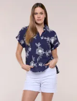 Blusa azul marino de corte amplio en tejido de puro algodón, con cuello camisero abierto en V y detalle de bordado floral en color blanco en toda la superficie. Cuenta con mangas cortas de hombro caído con puño doblado fijo y ruedo curvo con espalda más larga.