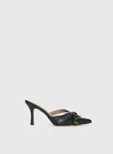 Mules de cuero negro con punta fina, diseño abierto en los laterales y tiras decorativas con ojales metálicos y hebilla ajustable.