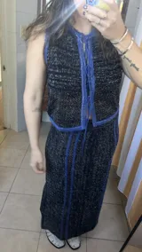 Chaleco tejido sin mangas, color negro, con textura brillante (lurex) y ribetes en azul. Presenta un escote redondo y se ata al frente con cordones.