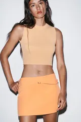 Top crop de tejido de punto color beige claro, con cuello redondo y manga sisa. Presenta acabados en rib en el cuello, sisas y bajo.