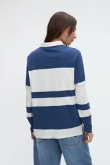 Remera polo de manga larga de algodón lavado, con diseño de rayas horizontales anchas en azul y blanco, cuello y cartera de botones en color blanco, y pequeños tajos laterales.