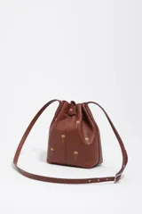 Bolso tipo bucket Bimba y Lola modelo Carlino, confeccionado en cuero marrón con estampado de pequeñas palmeras doradas y logo impreso en la parte frontal. Cuenta con cierre de cordón ajustable y asas largas para llevar al hombro.