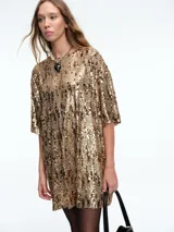 Vestido corto de corte recto y holgado, confeccionado en tejido cubierto de lentejuelas doradas. Presenta cuello redondo, mangas cortas amplias y una caída fluida.