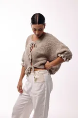 Saco de punto gris con frente abierto, cierre mediante lazos frontales y mangas con puños elásticos. Presenta una textura suave y un diseño de volumen holgado.