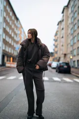 Anorak corto acolchado color marrón chocolate, con cuello subido, manga larga con puños elásticos y cierre frontal con botones ocultos y lazada lateral.