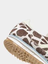 Championes Adidas modelo SL 72 OG con diseño de perfil bajo. Presentan una parte superior de piel con acabado de pelo de poni con estampado animal print de manchas marrones y blancas. Incluyen las icónicas tres tiras laterales en color crema, cordones celestes y suela de goma con entresuela de EVA.