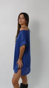 Vestido corto de tejido liviano con acabado brillante y caída fluida. Presenta un diseño holgado con escote amplio, mangas cortas y tajos laterales en el ruedo. Incluye forro interno para mayor comodidad.