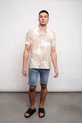 Camisa de manga corta con estampado de hojas en tonos beige y blanco, con cuello clásico y cierre frontal con botones.