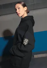 Buzo negro oversize de frisa con capucha amplia, bolsillo canguro, terminaciones de puño y ruedo con rib, y logo bordado en el centro delantero.