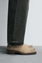 Bota cowboy de caña media, color beige claro con efecto desgastado. Fabricada en piel serraje engrasado, presenta horma cuadrada y tacón ancho de madera a contraste.