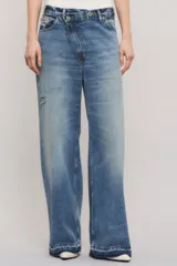 Jeans de denim azul con calce holgado y tiro medio, con diseño de cintura asimétrica cruzada, roturas localizadas y ruedo desflecado con degradé.