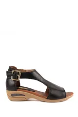 Sandalia baja de cuero negro con tira en T y hebilla metálica dorada en el talón. Posee suela de goma color camel con diseño anatómico.