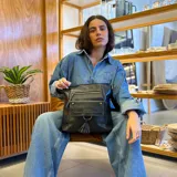 Bandolera negra de cuero sintético con cierre superior y correa larga regulable. Tiene bolsillo frontal con tapa y broches magnéticos, detalle de trenza artesanal, división interna, bolsillos internos y bolsillos laterales tipo ojal.