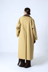 Trench color beige con cuello camisero, doble botonadura frontal, cinturón y bolsillos laterales.