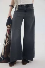 Pantalón jean gris oscuro de tiro medio y piernas anchas, con diseño de cinco bolsillos y cierre frontal con botón y cremallera.