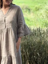 Vestido corto de lino color beige claro, con cuello mao, escote con botones de nácar, mangas tres cuartos con volados y ruedo con volado.