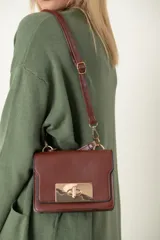 Cartera marrón de imitación cuero, pequeña con broche metálico dorado, con asa corta para llevarla en la mano y larga para llevarla colgada.