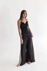 Pantalón de lino negro, de piernas anchas con cadera al cuerpo y cintura media. Tiene apliques triangulares de lino rayado en los costados.