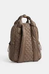 Mochila matelaseada de color marrón, con diseño acolchado de rombos, asas superiores con nudos y detalles en tono tostado. Cuenta con un bolsillo frontal con cierre, bolsillos laterales de red y un llavero decorativo con pompones y borla negra.
