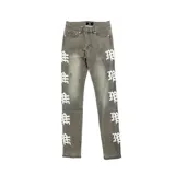 Pantalón de jean color gris lavado con diseño de monograma estampado en color blanco a lo largo de ambas piernas. Presenta un corte ajustado, cierre frontal con botón y bolsillos laterales.